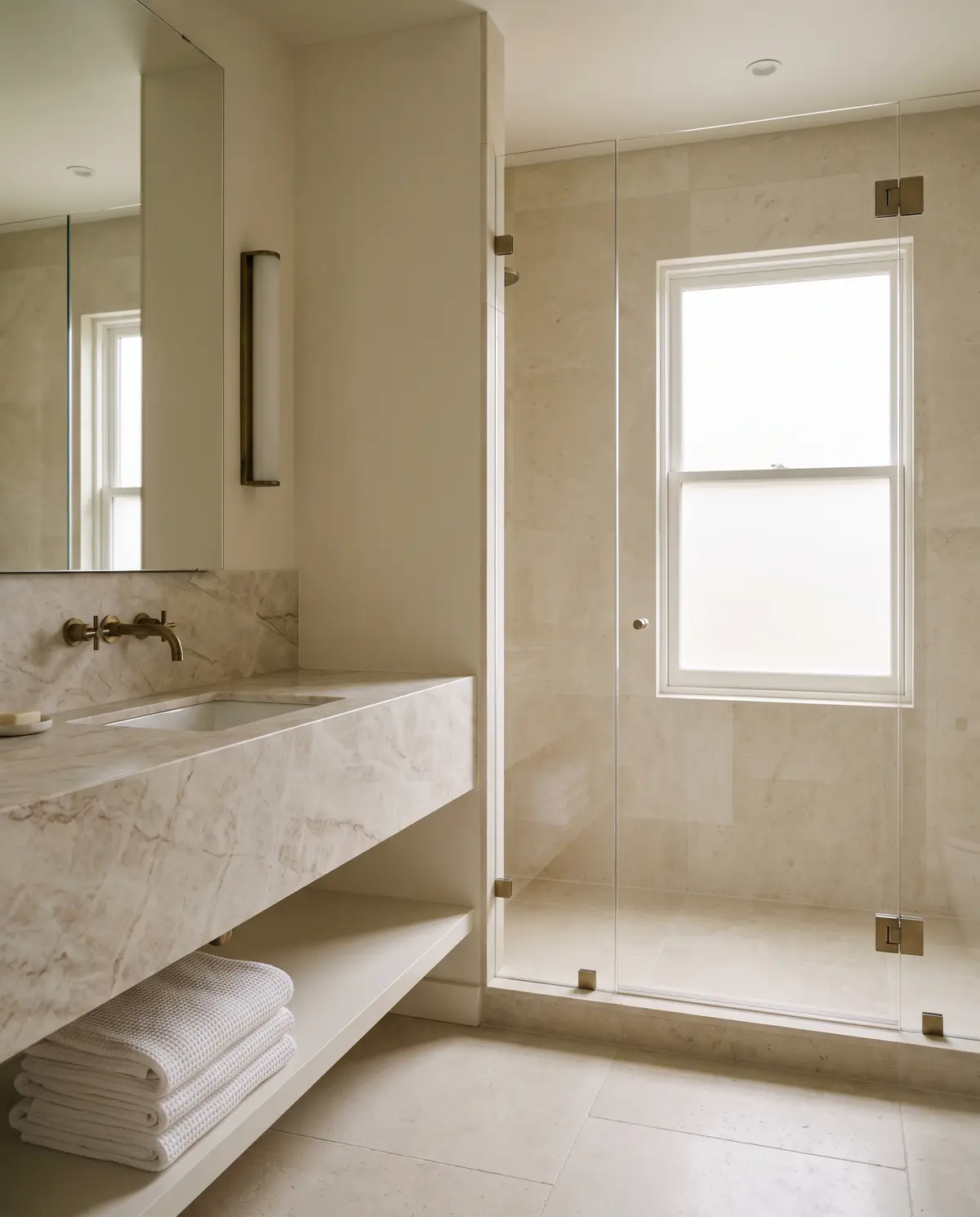 A calm bathroom with a marble vanity, frameless glass shower and folded white towels