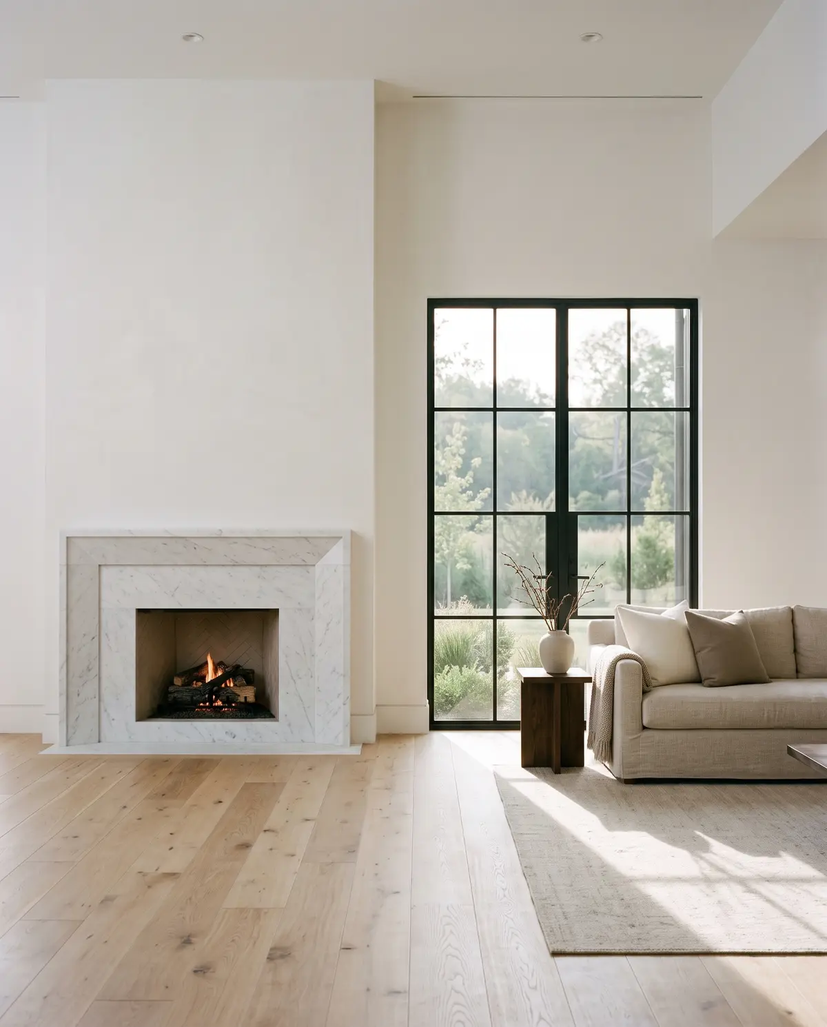 A calm living room with a marble fireplace and white oak floors in morning light
